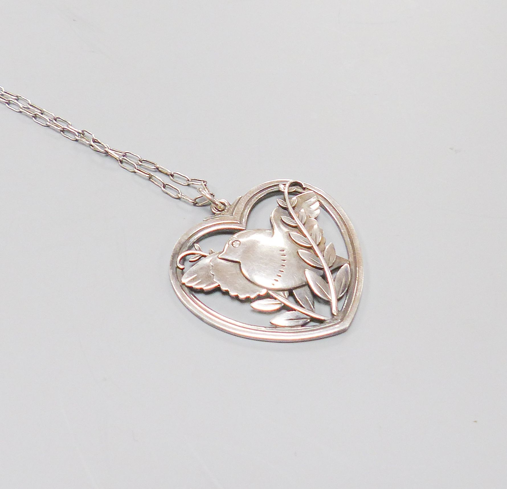 A Georg Jensen sterling 'Robin and frond' heart shaped pendant, no. 97, 38mm, on a white metal chain, 57cm.